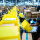 A Amazon warehouse worker stands by a conveyor belt as they put packages onto the line.